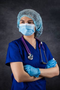 Cerrahi maske takan kadın doktor ya da hemşire portresi ve karanlıkta izole edilmiş steteskoplu eldivenler. Kadın hastane çalışanı kameraya, sağlık hizmetlerine bakıyor.