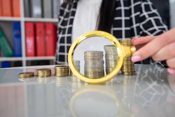 female holds magnifying glass over stacks of coins euro or dollar.  Investment search concept