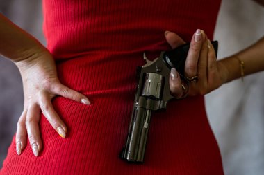 young woman in red dress holding gun pistol. crime concept. back view