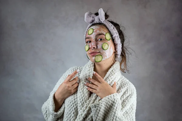 Young woman applying  facial cleanser mask with cream and slices of cucumber. Health of her skin