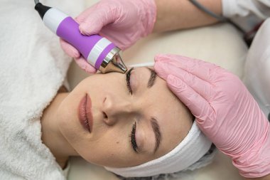 Kaplıca salonunda yalan söyleyen genç bir kadın. Yüzüne fonoforez ultrason cihazıyla temizlik yapılıyor. Yaşlanma karşıtı kozmetik işlem