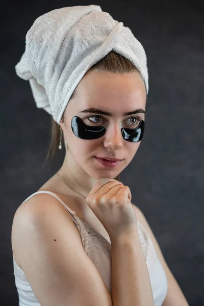 黒い壁に目の下にコラーゲンの黒い目のパッチを適用する魅力的な若い女性 美容ケアのための天然化粧品 — ストック写真