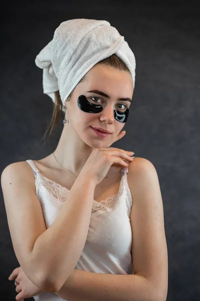 タオルの女性は黒を背景に目の下に美容パッチを適用します 美容化粧品 — ストック写真