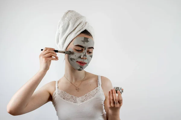 woman in towel with brush applied a black cleansing mask on face isoalted on white. Cosmetic mask as anti aging treatment