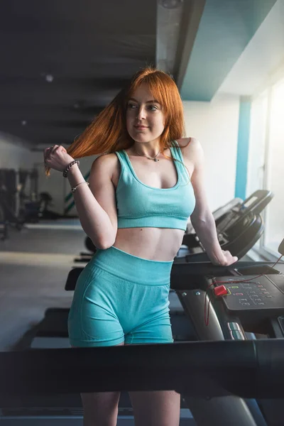 young skinny sporty female athletic stand near  treadmill trainers and rest after exercise at gym. Sport for all