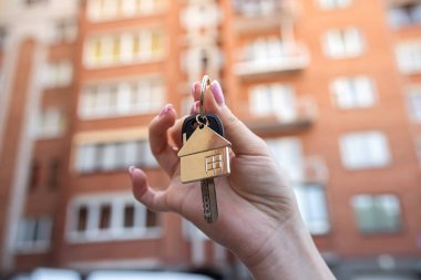 Güzel genç kadın elleri binanın arka planında yeni dairenin anahtarlarını tutuyor. Daire satın alma fikri. Anahtarlar elinde. Yeni apartman yerleşimi