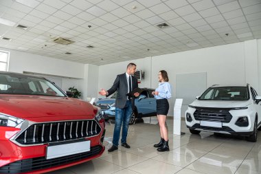 Genç adam yeni bir araba galerisine geldi ve kadın bir danışmanla yeni araba markaları hakkında konuştu. Araba satın alma kavramı