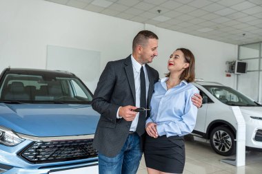 an extremely happy woman is happy when her husband bought a car at a car dealership. happy couple in salon. car purchase