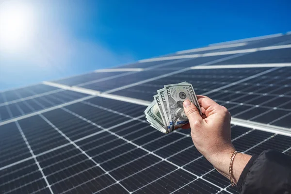 Saving money with solar energy and solar panels. Hand with dollars in front of panels. the concept of saving electricity