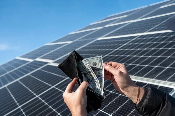 Money dollars in a wallet holding hands over a solar panel. Banknotes on the panel. Concept of cheap solar energy.