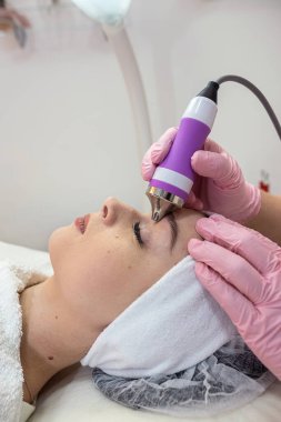 Yüzüne alet fonoforezi uygulayan genç bir kadın. Donanım yüz temizleme prosedürü. 