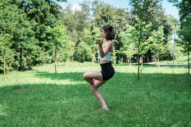 Açık hava parkındaki yeşil çimlerde egzersiz yapan beyaz bir kadın. Sağlık için spor