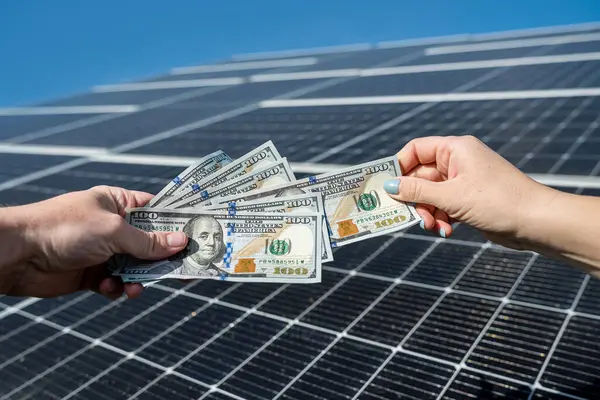 one hand hands another dollar for installing solar panels in his yard. payment of work installation of solar panels