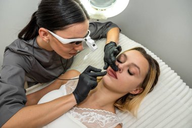 Kadın doktor, istenmeyen sakalların kalıcı olarak alınması için elektroepilatör kullanır. Defilasyon ve güzellik kavramı