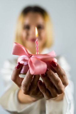 Bornozlu beyaz bir kadın elinde doğum günü mumu olan bir kek tutuyor. Sade bir zeminde izole edilmiş. Doğum günü. Tatil. Selamlama