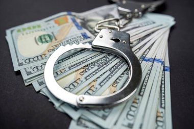 Kelepçe 100 dolarlık Amerikan banknotlarına dayanıyor. Siyah arka planda izole edilmiş. Yolsuzluk, soygun ve dolandırıcılık kavramı