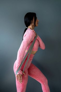 Gri arka planda direniş bandıyla egzersiz yapan beyaz bir kadın. Ev çalışması