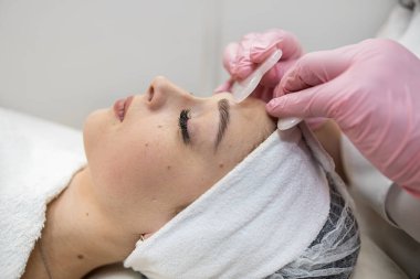 Kozmetik uzmanı müşterinin yüzüne beyaz guaj kazıyıcı sürerek tıbbi işlem yapıyor. Sağlık yaşam tarzı