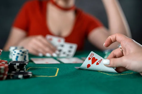 beautiful young girl sits at a poker table with cards in her hands and a player opposite. poker game of chance. woman\'s hands hold poker cards.