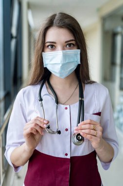 Portrait of female medical worker holding patient documents and stethoscope around neck in face mask and headgear for protection. The concept of medical workers. Portrait of a doctor