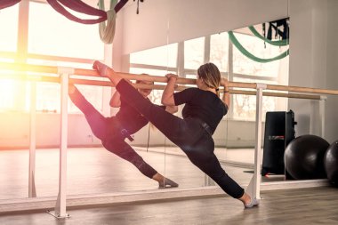 Kız, büyük aynaları olan parlak bir stüdyoda dikey yarıklar açmak için egzersiz yapıyor. Tel. Spor. esneme