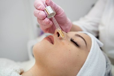Güzellik uzmanlarının ellerine yakın çekim, kaplıca salonundaki genç kadınların yüzüne pipetle birkaç damla yağ damlatıyor. Yüz dermatolojisi prosedürü, cilt bakımı