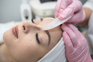 Gua Sha taş aletle yüz masajı yapıyor. Güzellik salonunda güzellik tedavisi. Temiz yüz teni kavramı 