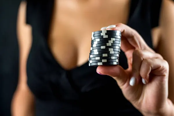 cropped portrait of woman in black dress holding chips in front of cleavage for gambling. Poker. Games for adults. Poker chips in female hands. isolated on black background