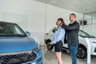 Beautiful man and woman couple holding key to their new car looking at camera and smiling in car showroom. purchase of a family car. new car showroom