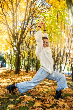 Gülümseyen genç kadın, sonbahar parkında güneşli havanın tadını çıkar, yaşam tarzı.
