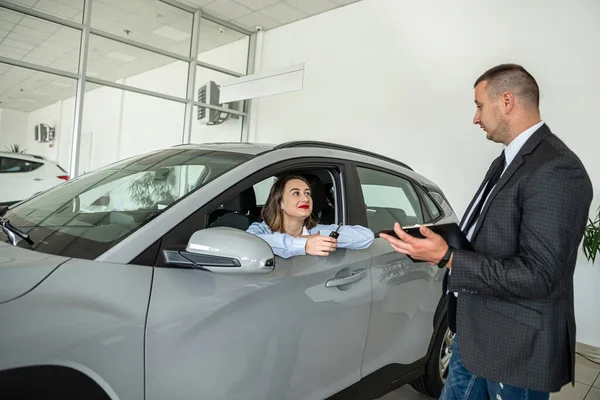 Young female business client talking with a sales man in a car showroom, sale or rent vehicle in showroom