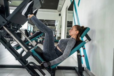 Spor kıyafetli bir kadının portresi spor salonunda gün içinde simülatörlerle fiziksel egzersiz yapıyor. Vücudu dayanıklılık için eğitmek. Sağlıklı Yaşam Tarzı