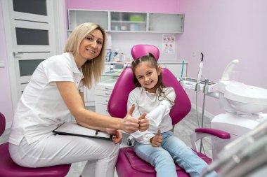 happy female dentist is interviewing a little girl patient in the office of a children's dental clinic. Dentistry technology. technology and healthcare concept. children's dentistry