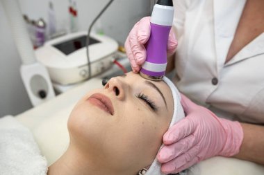 Güzellik uzmanı, kaplıcadaki kadın yüzünde fonoforez donanım ile temizlik prosedürü yapıyor. Gençleştirme prosedürü, cilt bakımı. 