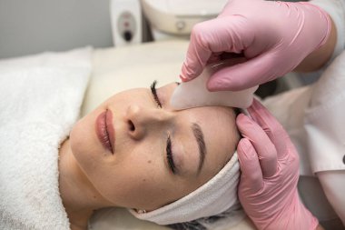 Kaplıca kliniğinde yüzü gua sha yeşim taşıyla masaj yaptıran genç ve güzel bir kadın. Vücut bakımı kavramı