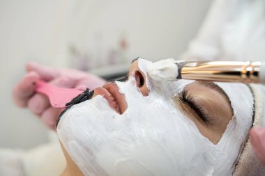 Genç bayan müşteri güzellik salonundaki beyaz maskeden yüz bakımı alıyor. Cilt bakımı kavramı