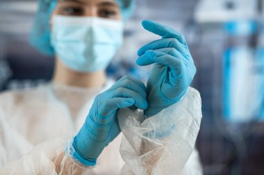 Genç bayan doktor ya da asistan cerrah ameliyathanede mavi koruyucu eldiven takıyor. Tıp ve sağlık hizmetleri kavramı