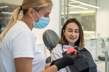 woman dentist shows on a model of the jaw how to properly brush the teeth with a toothbrush and the patient girl heard the doctor correctly. healthy teeth jaw model. clipart