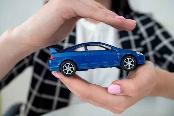 Closeup of female hands for protection small toy car at office.  Business concept