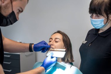 Profesyonel pratikte, dişçi hastanın dişlerini doktordan leke yaparak beyazlatma seviyesini kontrol eder. Konsept: dişçiler. Sağlık hizmeti. Mükemmellik. beyaz.