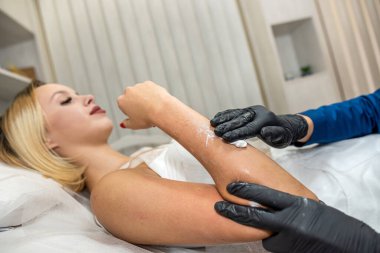 Usta shugaring, genç müşterisinin koluna kalın şeker yapıştırıcısı sürüyor. Sıvı şeker macunuyla coşmuş. Balmumu ya da şekerleme