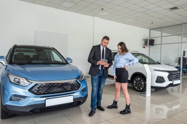 professional consultant provides all information about a new car using a tablet to his client at a car dealership