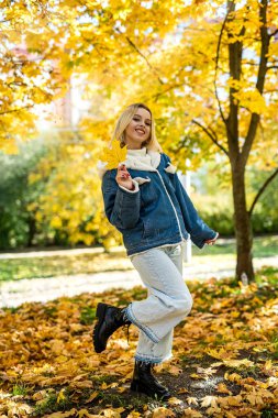 Gülümseyen genç kadın, sonbahar parkında güneşli havanın tadını çıkar, yaşam tarzı.