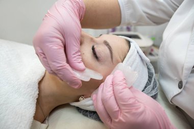 Kaplıca kliniğinde yüzü gua sha yeşim taşıyla masaj yaptıran genç ve güzel bir kadın. Vücut bakımı kavramı