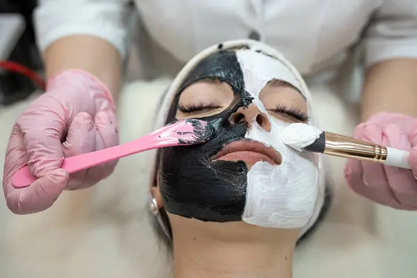 Woman with  black and white  mask of half face  at spa salon. Beauty procedures. Skin care