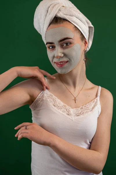 young woman applying green clay mask isolated on green. Beauty treatment, anti aging procedures