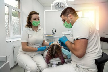 İki dişçi, bir erkek ve bir kadın ağzını açık tutan güzel bir kadın hastanın hasta dişlerini tedavi eder. Oral sağlık. dişler