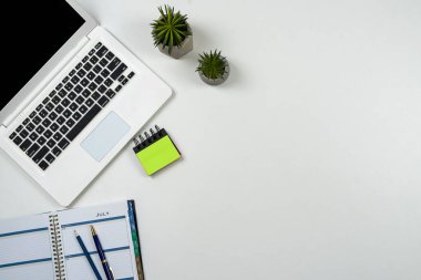 Beyaz ofis masasında kalem ve defter olan bir laptop. Düz yatış, üst görünüm