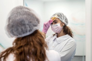 Aynanın yanında maske takmak için kemikleri olan bir güzellik uzmanı. Kozmetoloji prosedürleri kavramı. güzellik küresi