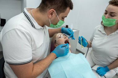 Gülümseyen dişçi ve bir asistan dişçi muayenehanesinde dişlerini kontrol ederken bir hastayla konuşuyor. dişçi dişleri